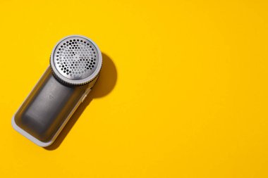 Elbiselere kumaş serpiştiren bir makine, sarı arka planda..