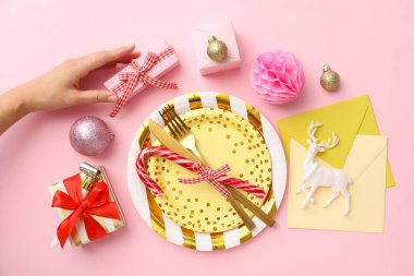 Tabaklar, çatal bıçak takımı, hediye kutuları, zarflar ve eller pembe arka planda.