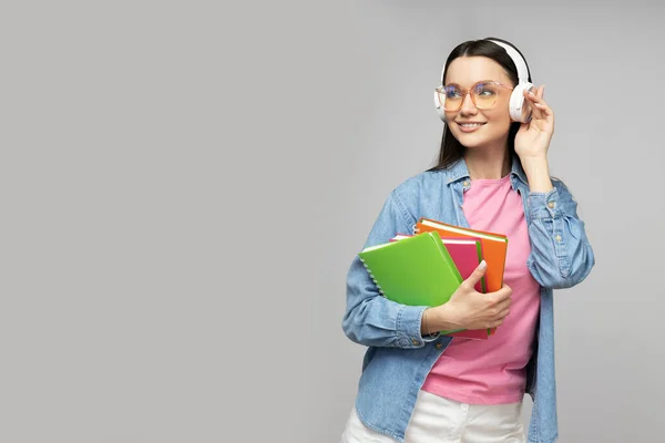 Attractive young woman in headphones and notebooks in hands