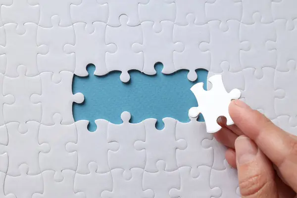 White puzzles and hand on blue background, top view