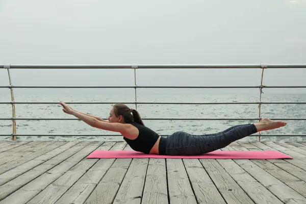 Woman on yoga mat on wooden floor at sea
