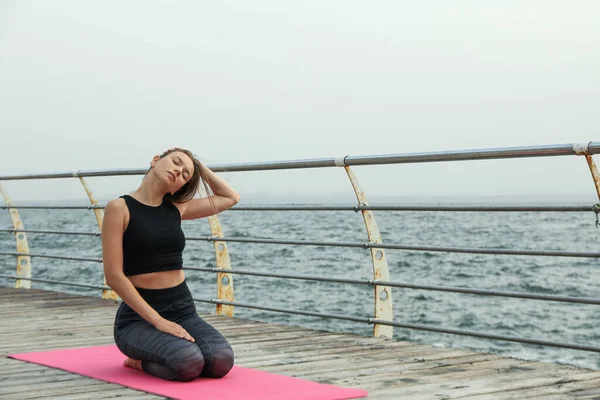 Woman on yoga mat on wooden floor at sea, space for text