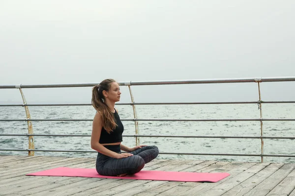 Woman on yoga mat on wooden floor at sea, space for text