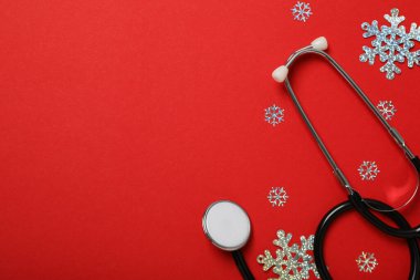 Kırmızı arka planda steteskoplu Noel kar taneleri