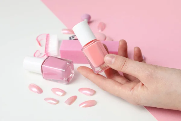 Manicure tools and nail polish in female hand on pink and white background, close up