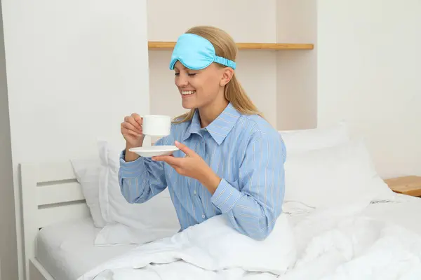 Young woman in sleeping mask drinking coffee in bed