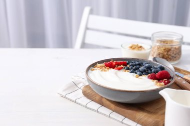 İçinde yoğurt ve böğürtlen olan bir kâse, hafif arka planda kaşık ve bir kavanoz yulaf ezmesi, mesaj için yer.