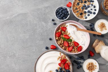 Yoğurt ve böğürtlenli kaseler, tahta kaşık ve gri arka planda süt şişesi, mesaj için yer