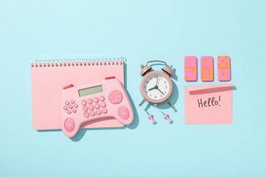 Alarm saati, not defteri, dominolar ve hesap makinesi mavi arkaplanda, üst görünümde.