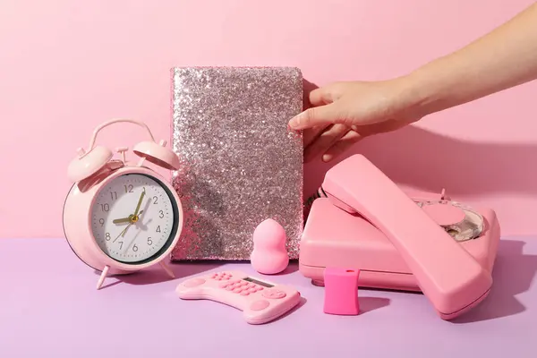 Phone, alarm clock, notepad in hand and calculator on pink background