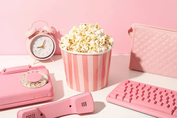 Alarm clock, phone, keyboard, bag and popcorn on pink background