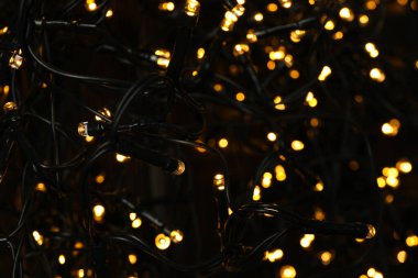 Ahşap zemin üzerinde sarı ışıklar olan siyah noel çelengi.