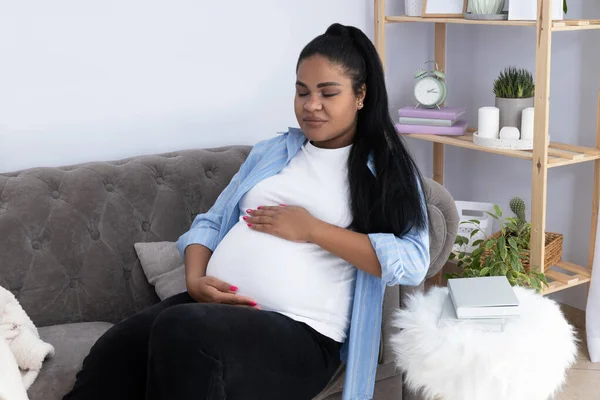 Pregnant African American woman in room on couch.