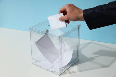 Kağıtlı oy sandığı ve mavi arka planda el.