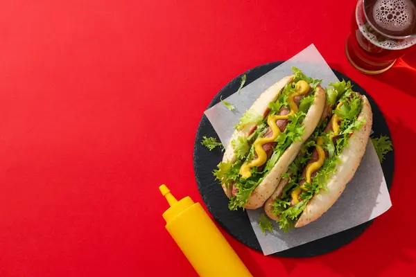 Hot dogs, sauce in bottle and glass on red background, space for text