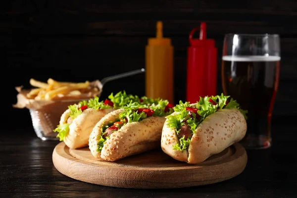 Hot dogs, sauces in bottles, glass and french fries on dark background