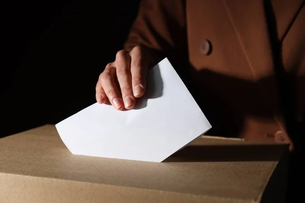Paper voting box and hand with paper on brown background, close up