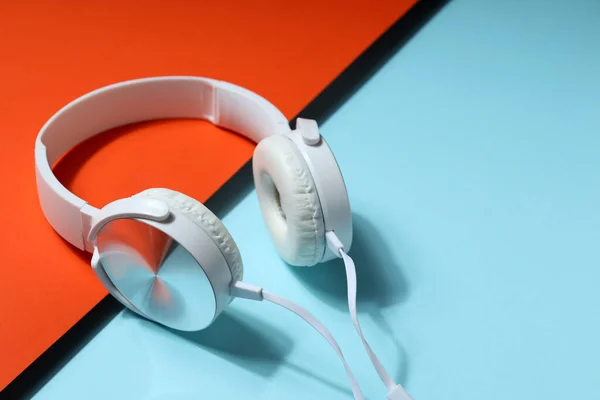 White, full-size wired headphones on a blue-orange background.