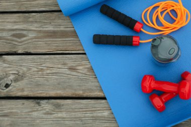 Yoga paspası, su şişesi, atlama ipi ve ahşap arka planda dambıllar, metin için yer