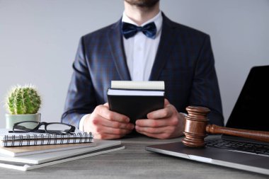 Takım elbiseli adam, not defterleri, tahta çekiç ve gri arka planda dizüstü bilgisayar.