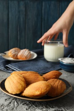 Madeleine kekleri, bir bardak süt ve el mavi ahşap arka planda, kapatın.