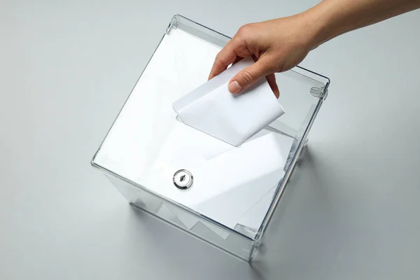 Voting box with papers and hand on gray background, top view