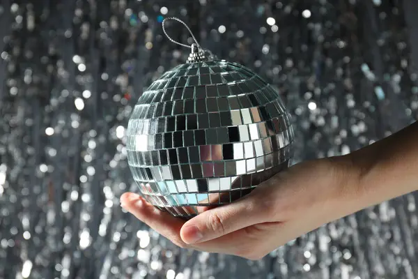 Disco ball in hand with festive silver ribbons on background