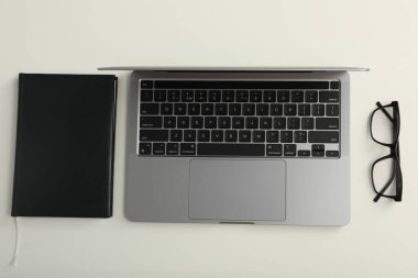 Dizüstü bilgisayar, gözlüklü ve not defterli.