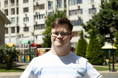 Down sendromlu bir çocuk yaz şehrinin arka planında poz veriyor.