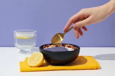 Buzlu kase, kadın eli kaşık ve mor arka planda bir bardak su.