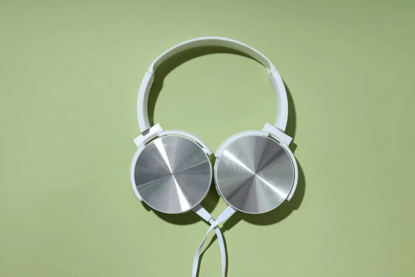White, on-ear headphones with a wire on a green background.