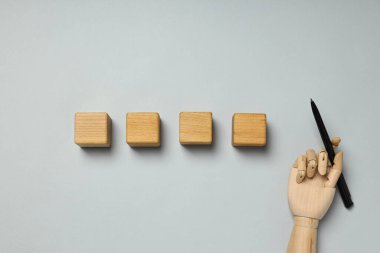 Ahşap küpler ve gri arka planda kalemi olan el, üst görünüm.