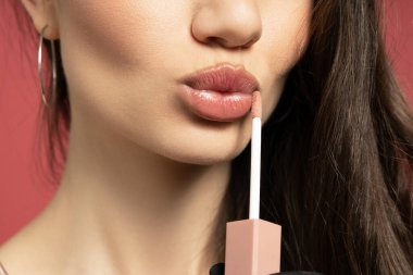 Çekici kız dudaklarını kırmızı arka plana boyuyor.