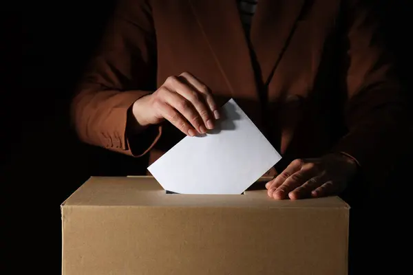 Paper voting box with form and men on black background, close up