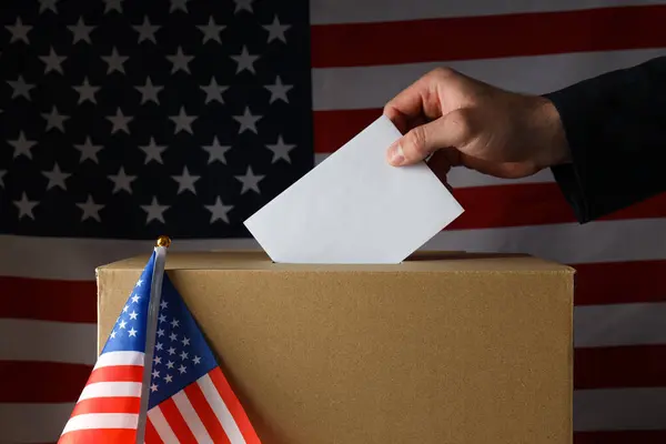 Paper voting box with paper and hand on american flag background