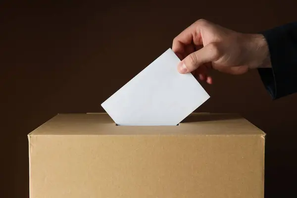 Paper ballot box with paper and hand on dark background