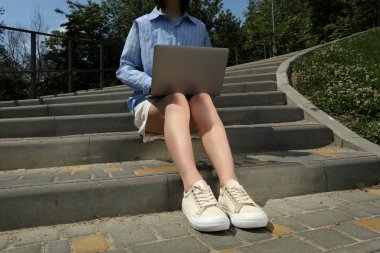 Kız merdivenlerde otururken dizüstü bilgisayarda çalışıyor.