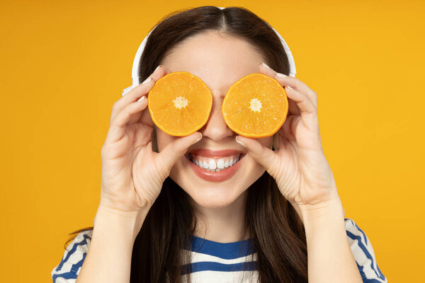 A girl in headphones with oranges in her hands, on a yellow background.