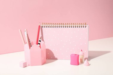 Not defteri ve kalemler pembe arka planda.