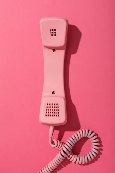 Pink telephone receiver on pink background, space for text