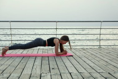 Yoga minderindeki genç kadın ahşap zeminde açık havada, mesaj için yer var.