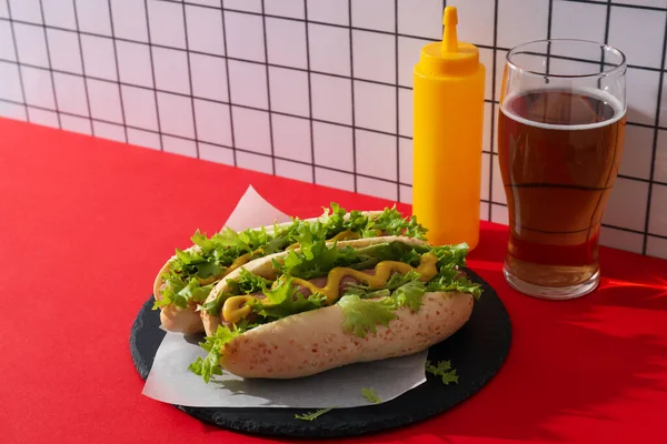 Hot dogs, sauce in bottle and glass on red table on light background