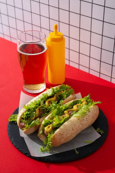 Hot dogs, sauce in bottle and glass on red table on light background