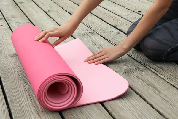 Female hands and pink yoga mat on wooden background
