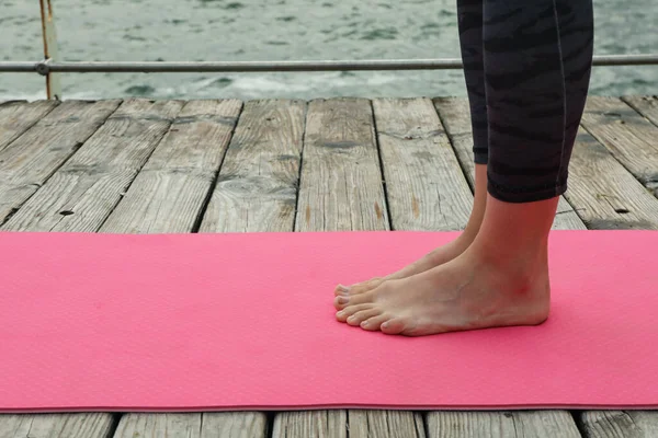 Female legs on pink yoga mat on wooden floor, space for text