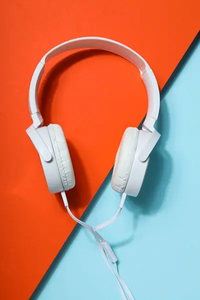 White, full-size wired headphones on a blue-orange background.