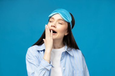 Mavi arka planda, uyku maskeli genç bir kadın.