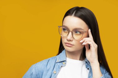 Gözlüklü güzel bir kız sarı arka planda poz veriyor.
