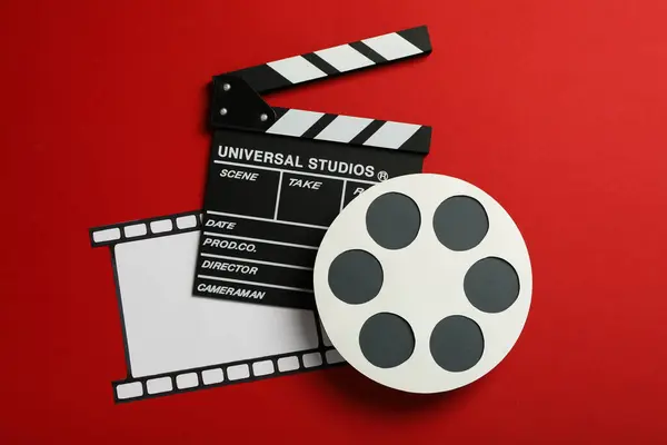 Clapperboard, paper reel and film on red background, top view