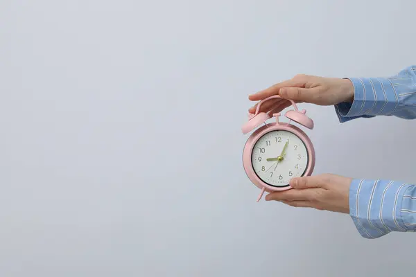 Pink alarm clock in hands on a light background